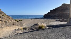 Naaktstrand Playa de Medio Almud is een donker zandstrand gelegen in een baai